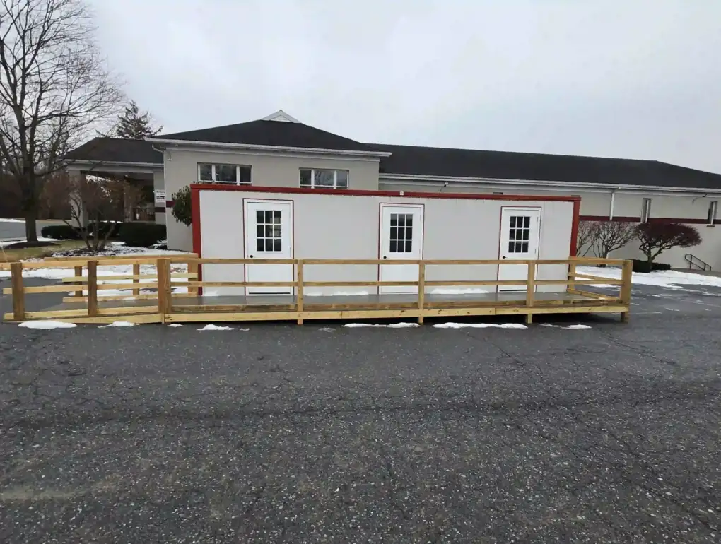Front view of an installed modular office featuring three doors and a full-length wooden wheelchair accessibility ramp.