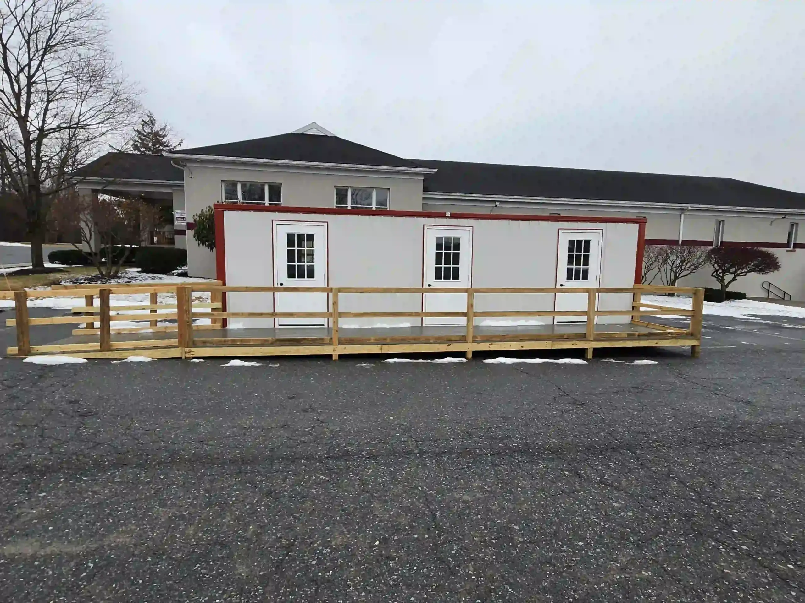 Front view of an installed modular office featuring three doors and a full-length wooden wheelchair accessibility ramp.