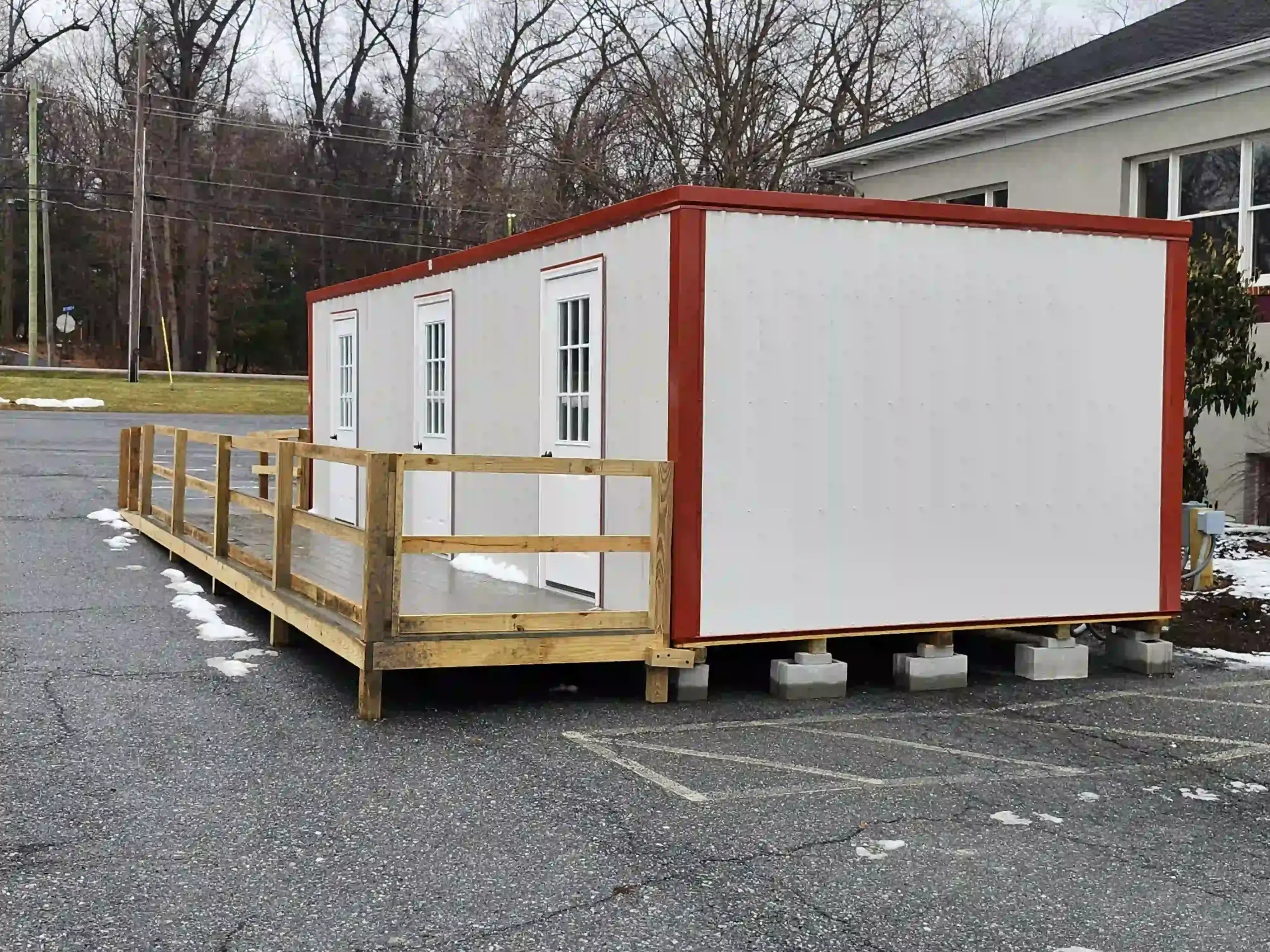 A portable office building installed on a sturdy foundation with a custom-built wooden ADA accessibility ramp.