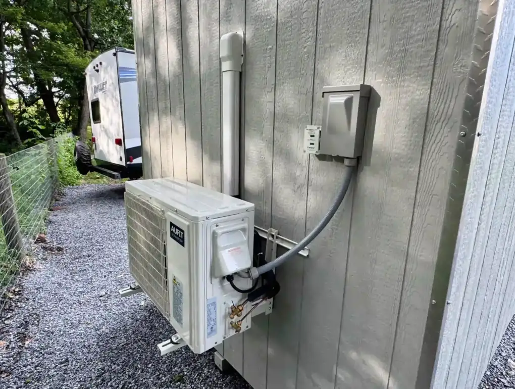 The exterior condenser and electrical hookup for a mini-split AC and heating system on a finished shed from Mill Run Storage.