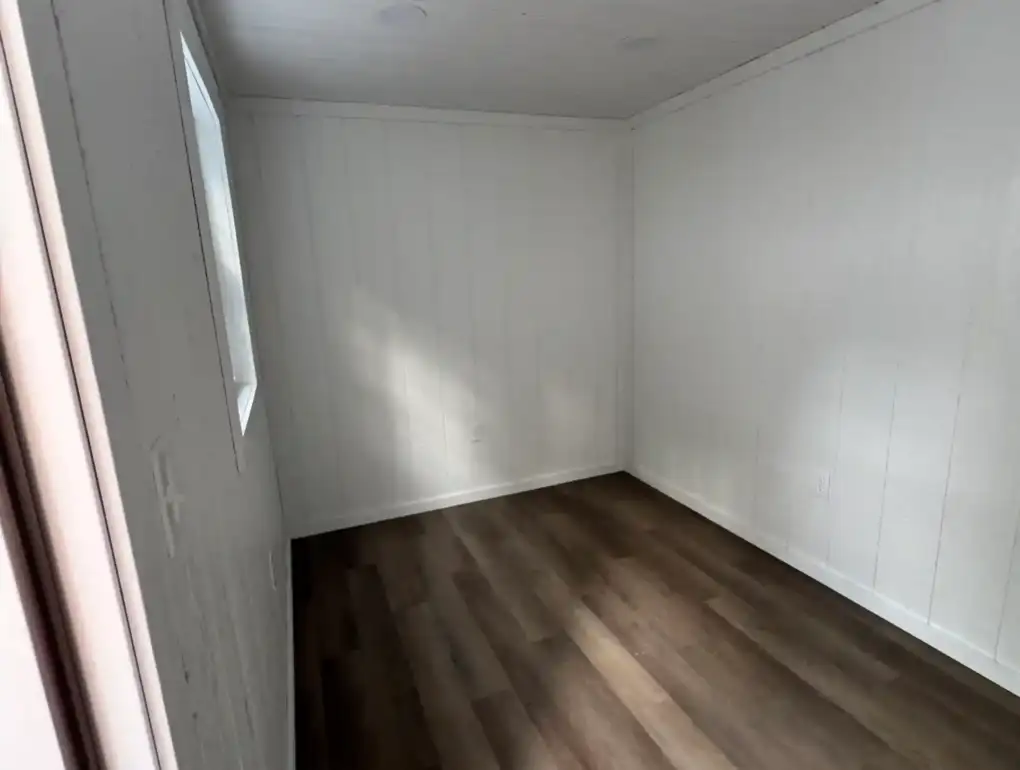 A bright, finished interior of a backyard studio shed, showcasing the clean walls, flooring, and electrical outlets ready for a home office.