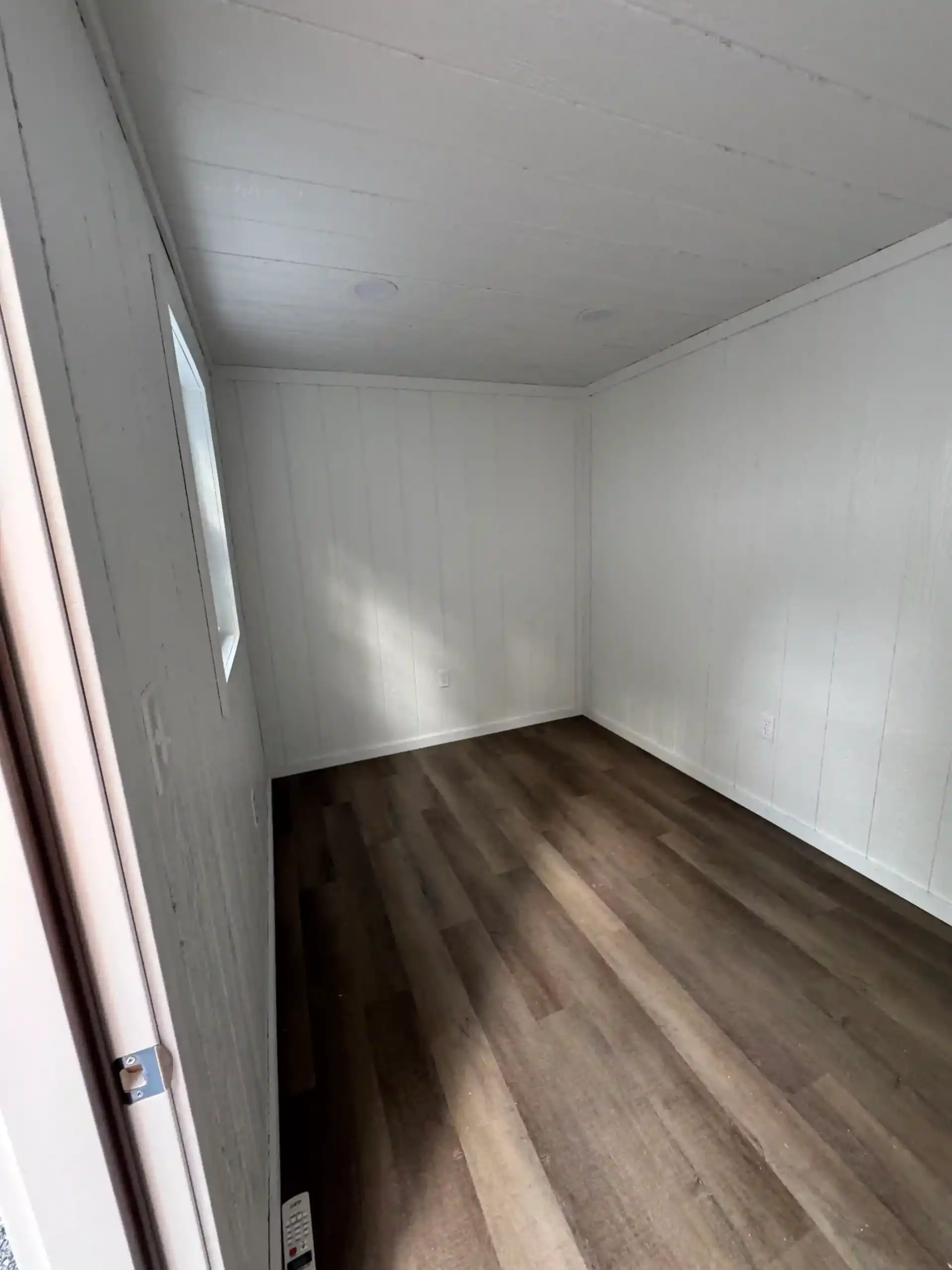 A bright, finished interior of a backyard studio shed, showcasing the clean walls, flooring, and electrical outlets ready for a home office.