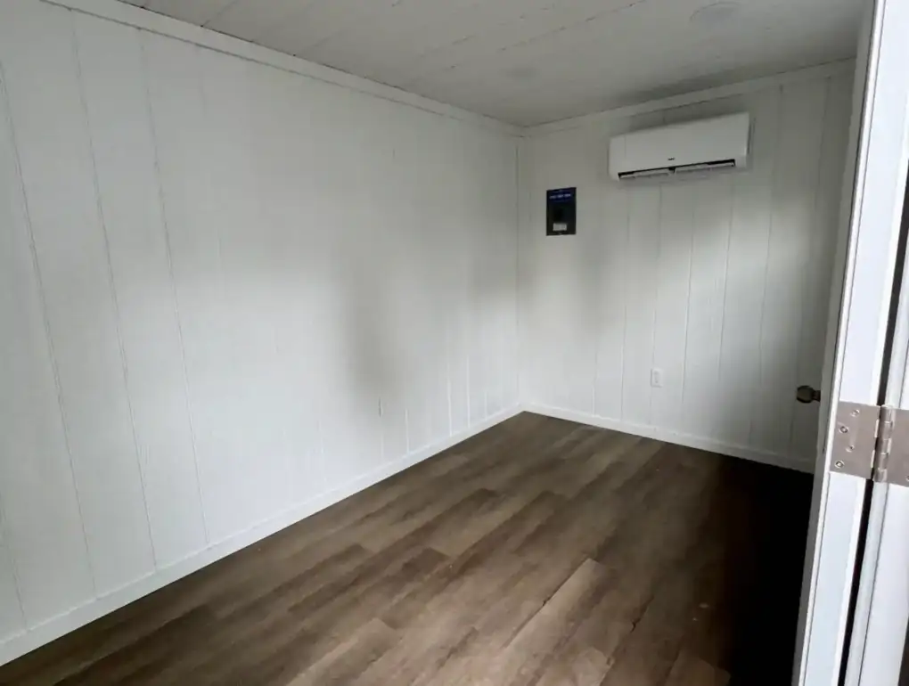 The fully finished interior of a portable office, featuring wood flooring, white walls, and a wall-mounted mini-split for year-round climate control.