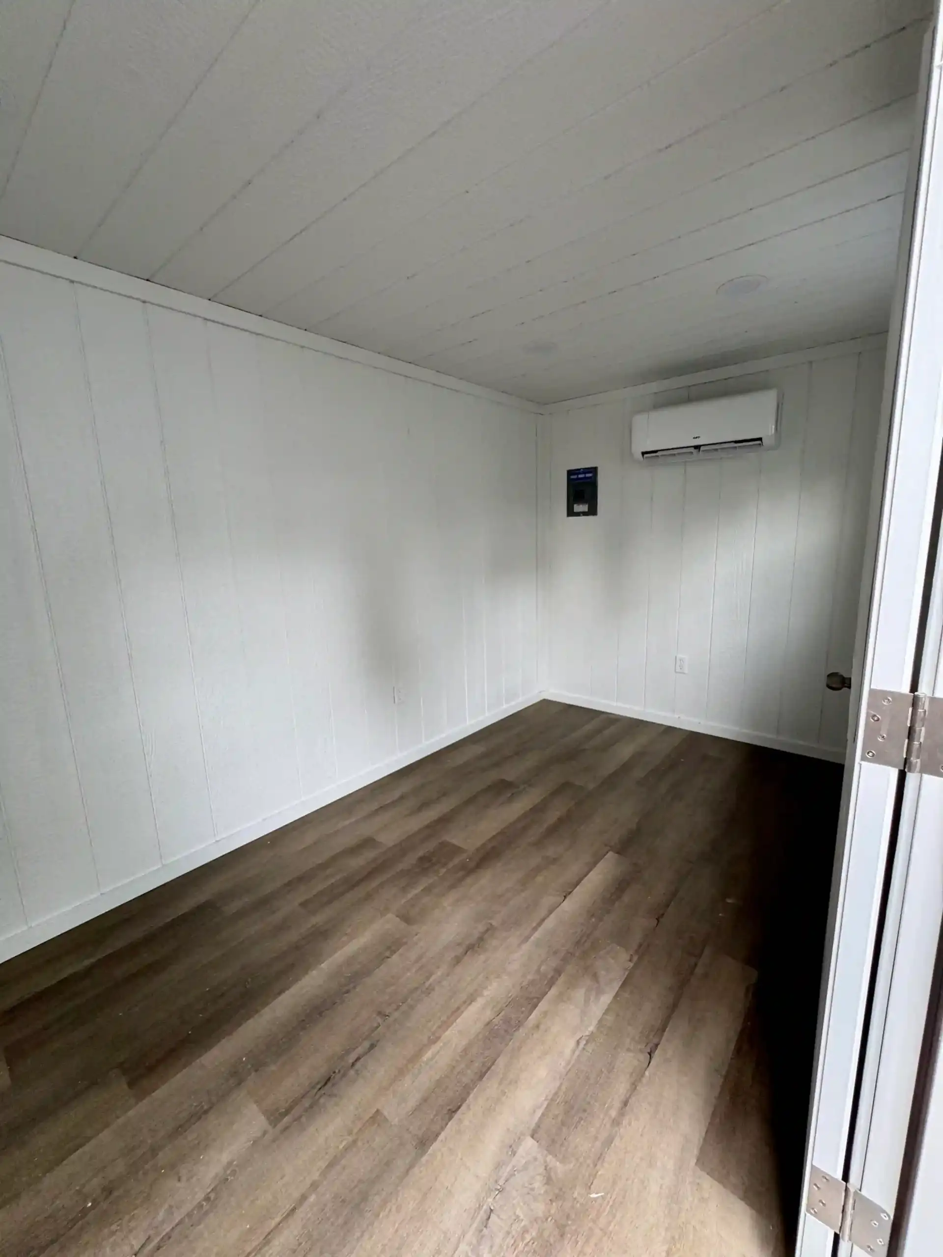 The fully finished interior of a portable office, featuring wood flooring, white walls, and a wall-mounted mini-split for year-round climate control.
