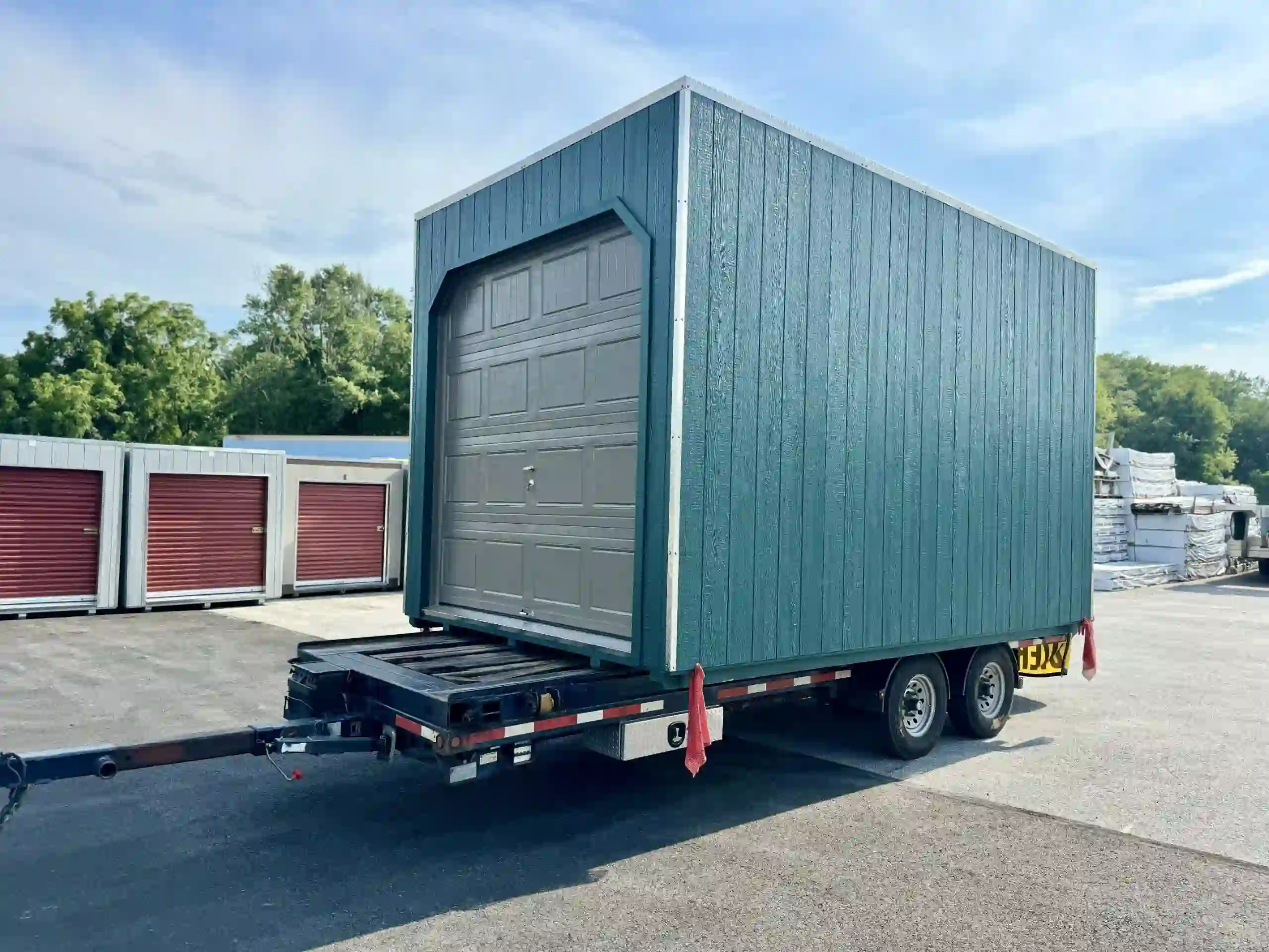 A green portable single-car garage with a gray overhead door, loaded on a trailer and ready for delivery in Pennsylvania.