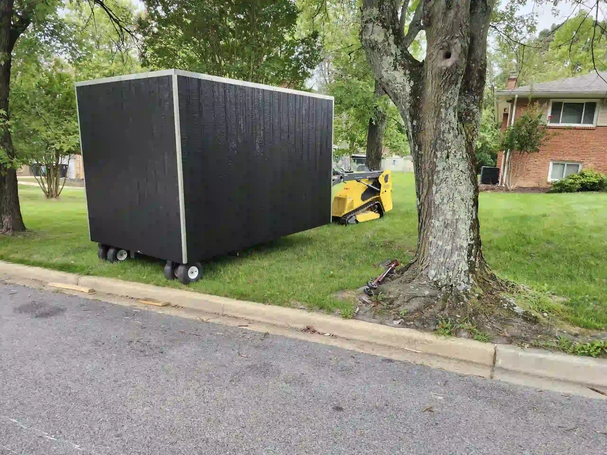 Our tracked shed mover carefully transports a storage unit across a lawn, demonstrating our yard-safe, no-damage delivery method.