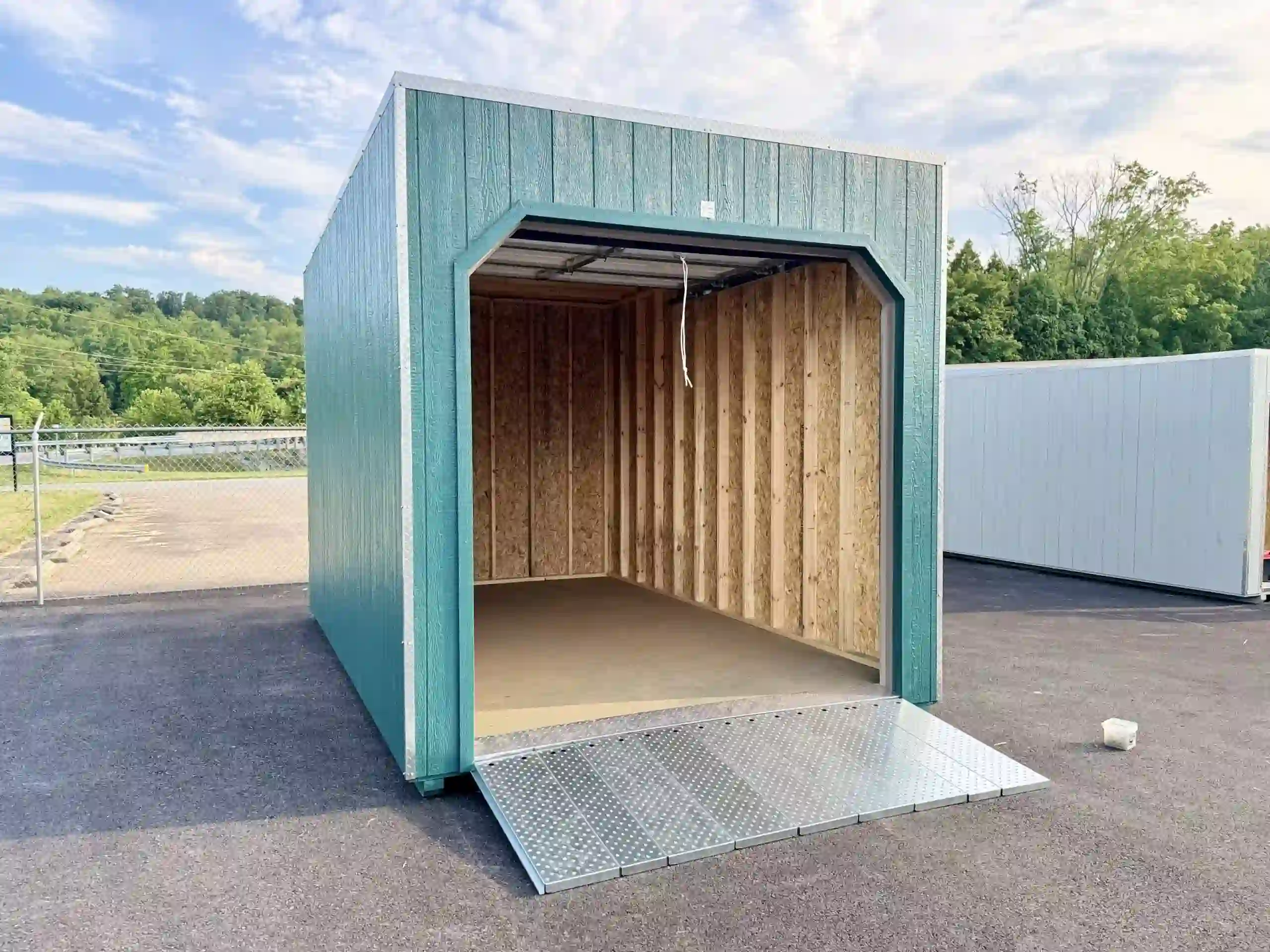 A portable garage with its door open and the heavy-duty, integrated metal loading ramp extended.