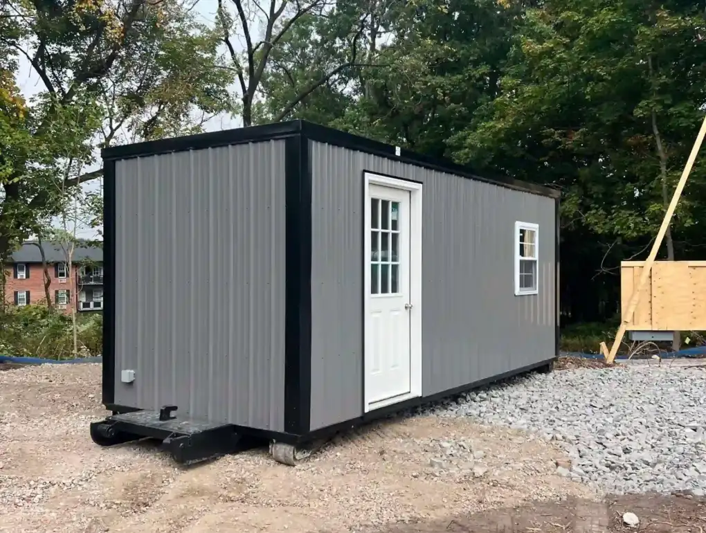 A durable metal-sided portable office being carefully positioned onto a prepared gravel pad with a shed mover.