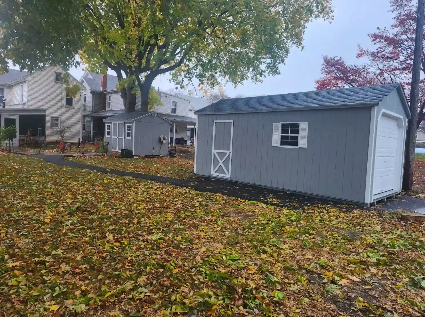 A new gray portable garage installed in a leafy Manheim backyard, providing ample space for vehicle and tool storage.
