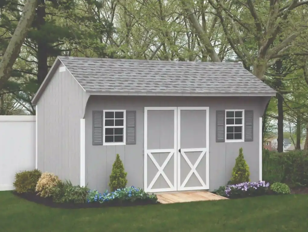 A classic gray wood storage shed with white crossbuck doors and gray shutters, perfect for any backyard in the Manheim or Christiana area.