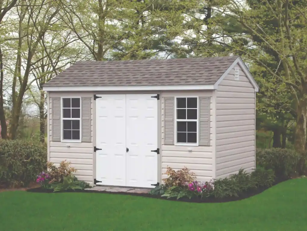 A low-maintenance beige vinyl storage shed with classic white double doors and gray shutters, available from Mill Run Storage.