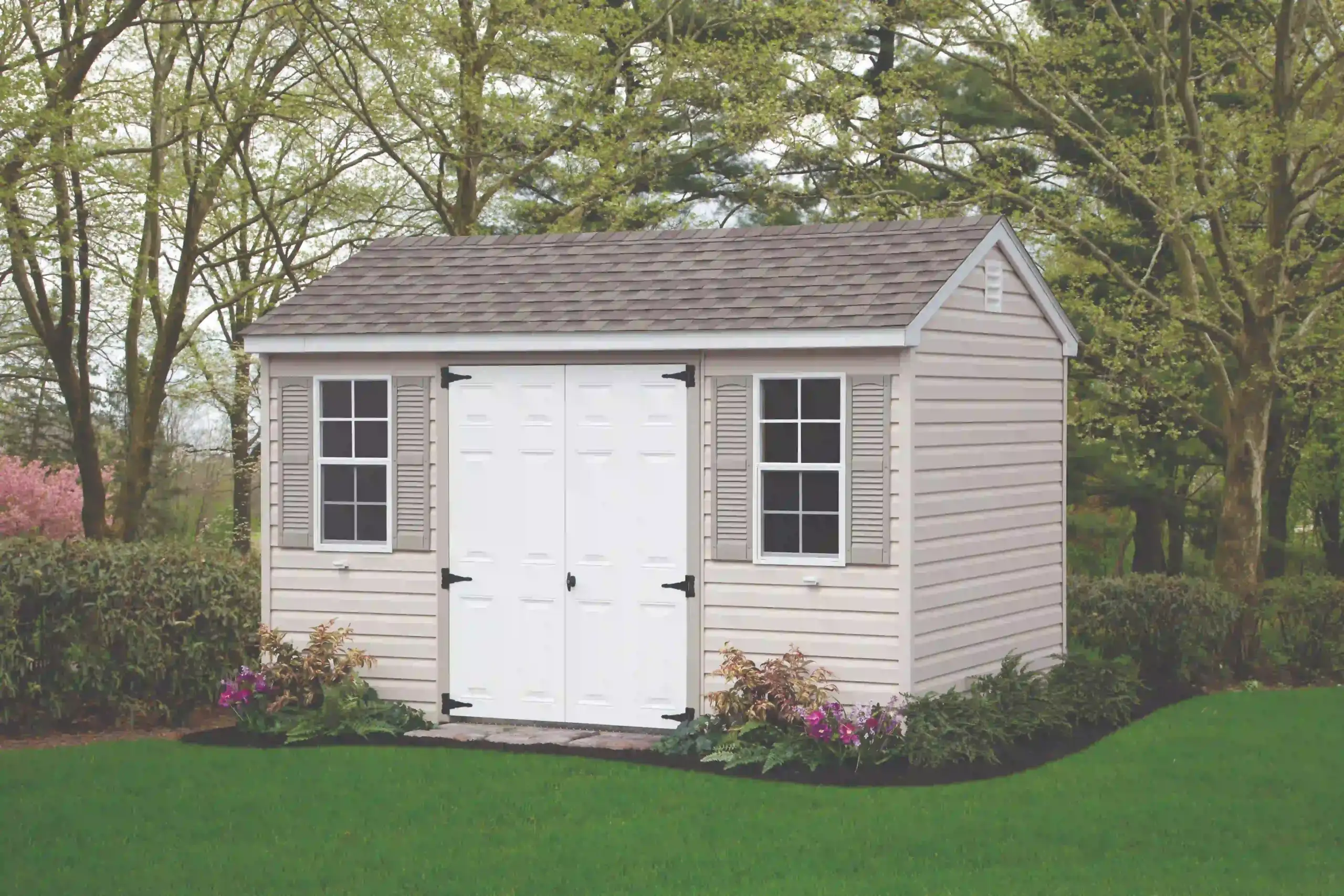 A low-maintenance beige vinyl storage shed with classic white double doors and gray shutters, available from Mill Run Storage.