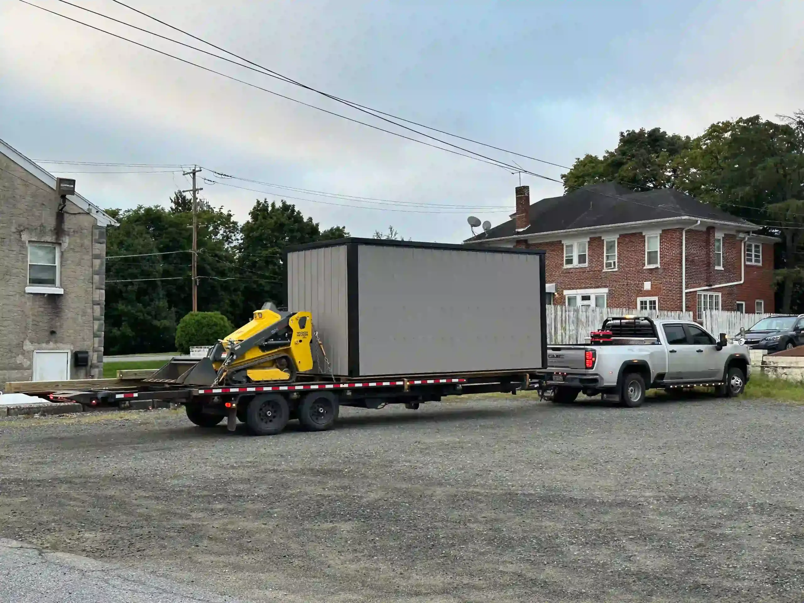 A modern metal office shed and placement equipment loaded on a trailer, ready for delivery from Mill Run Storage.