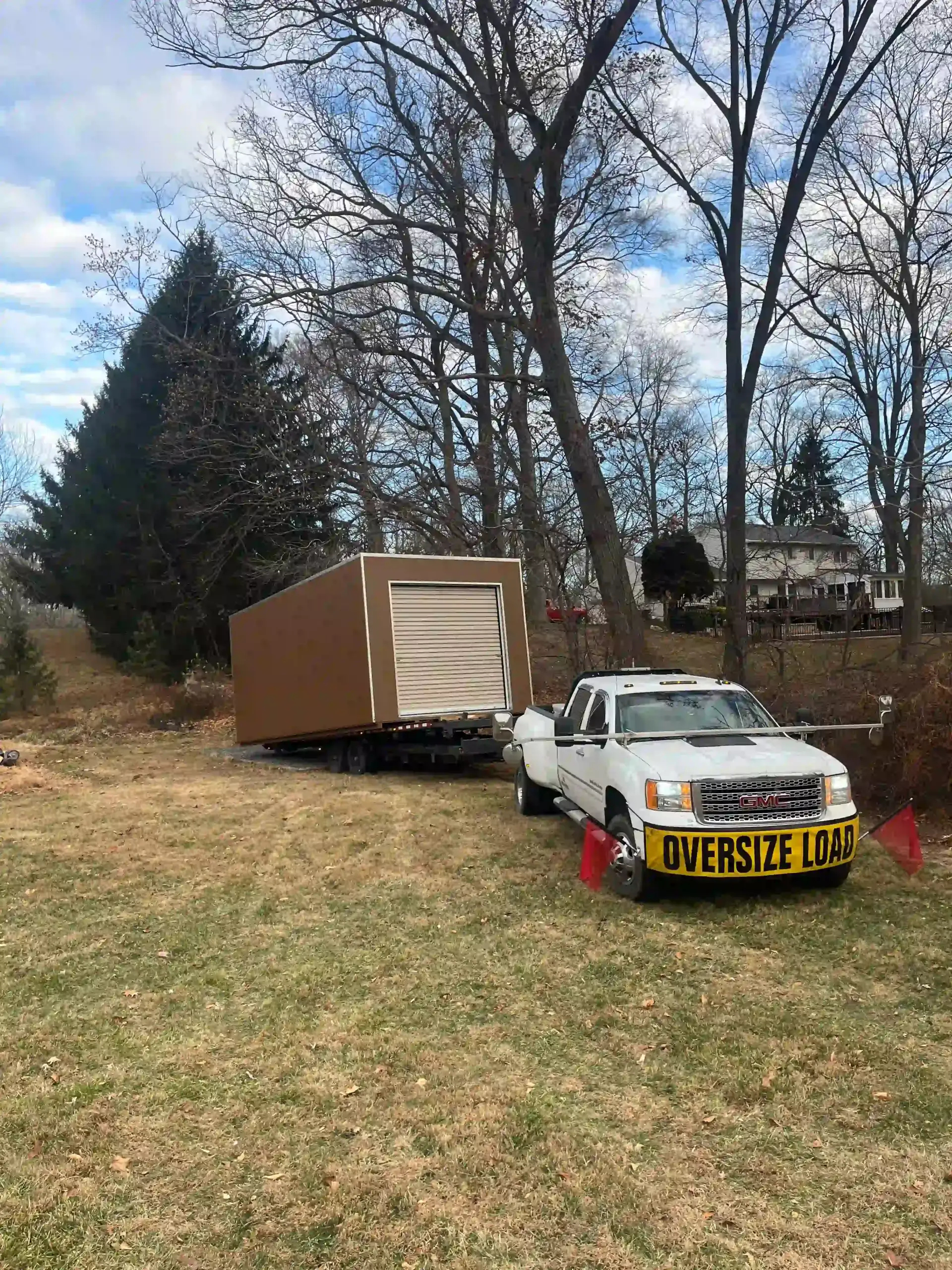 The Mill Run Storage delivery team carefully maneuvering a large portable storage unit with an "Oversize Load" truck into a customer's backyard.