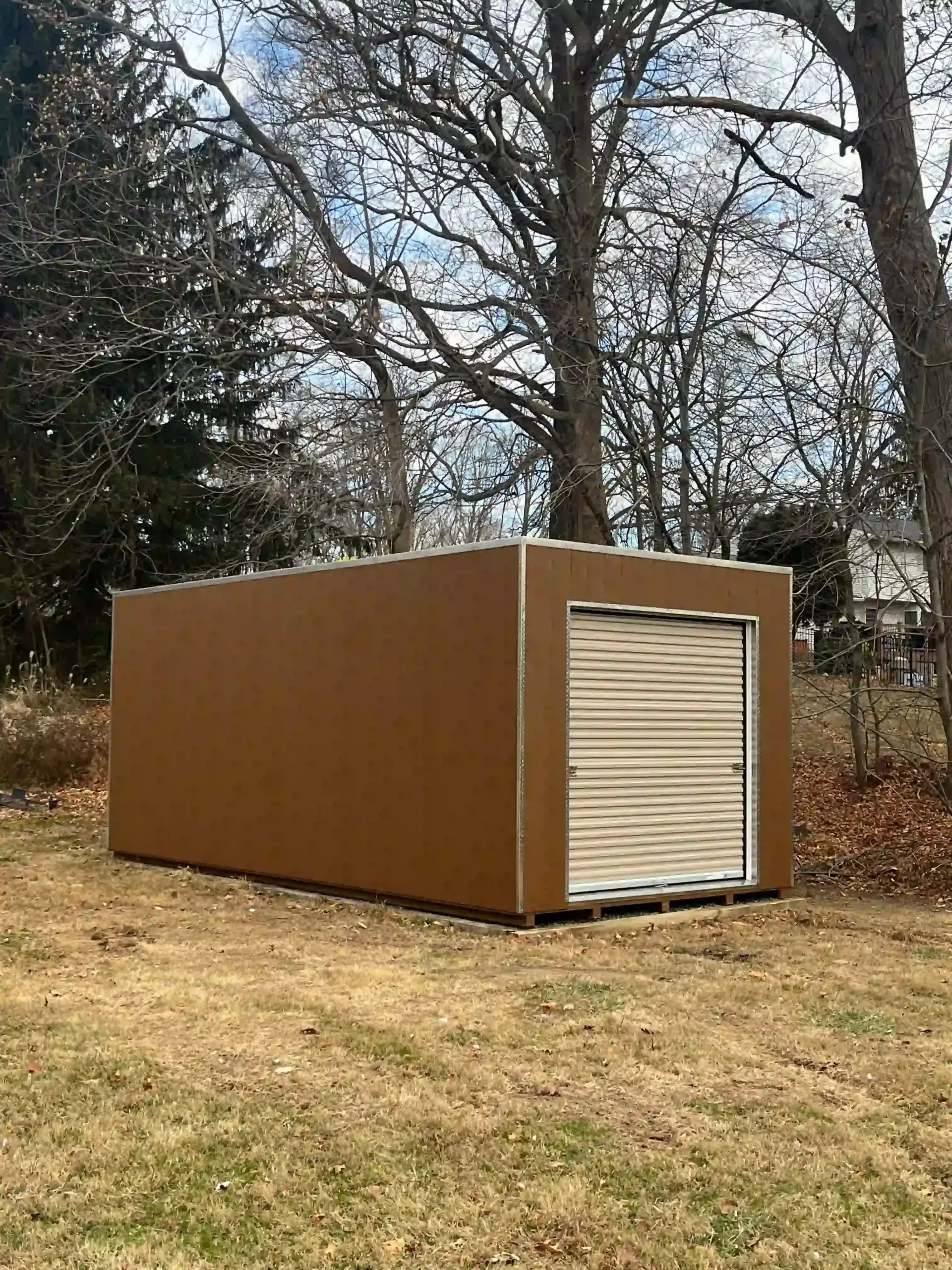 A brown, single-car portable garage with a roll-up door, successfully installed in a customer's backyard by the Mill Run Storage team.