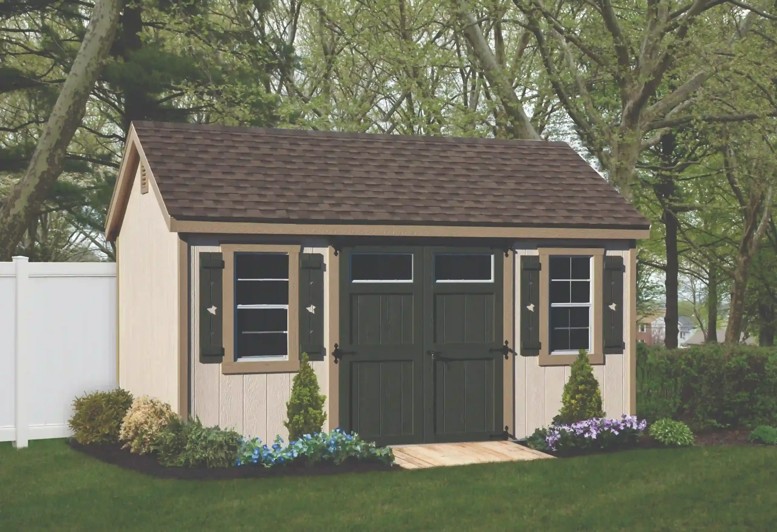 A workshop-style shed with cream siding, dark green shutters, and matching doors that feature transom windows for extra light.