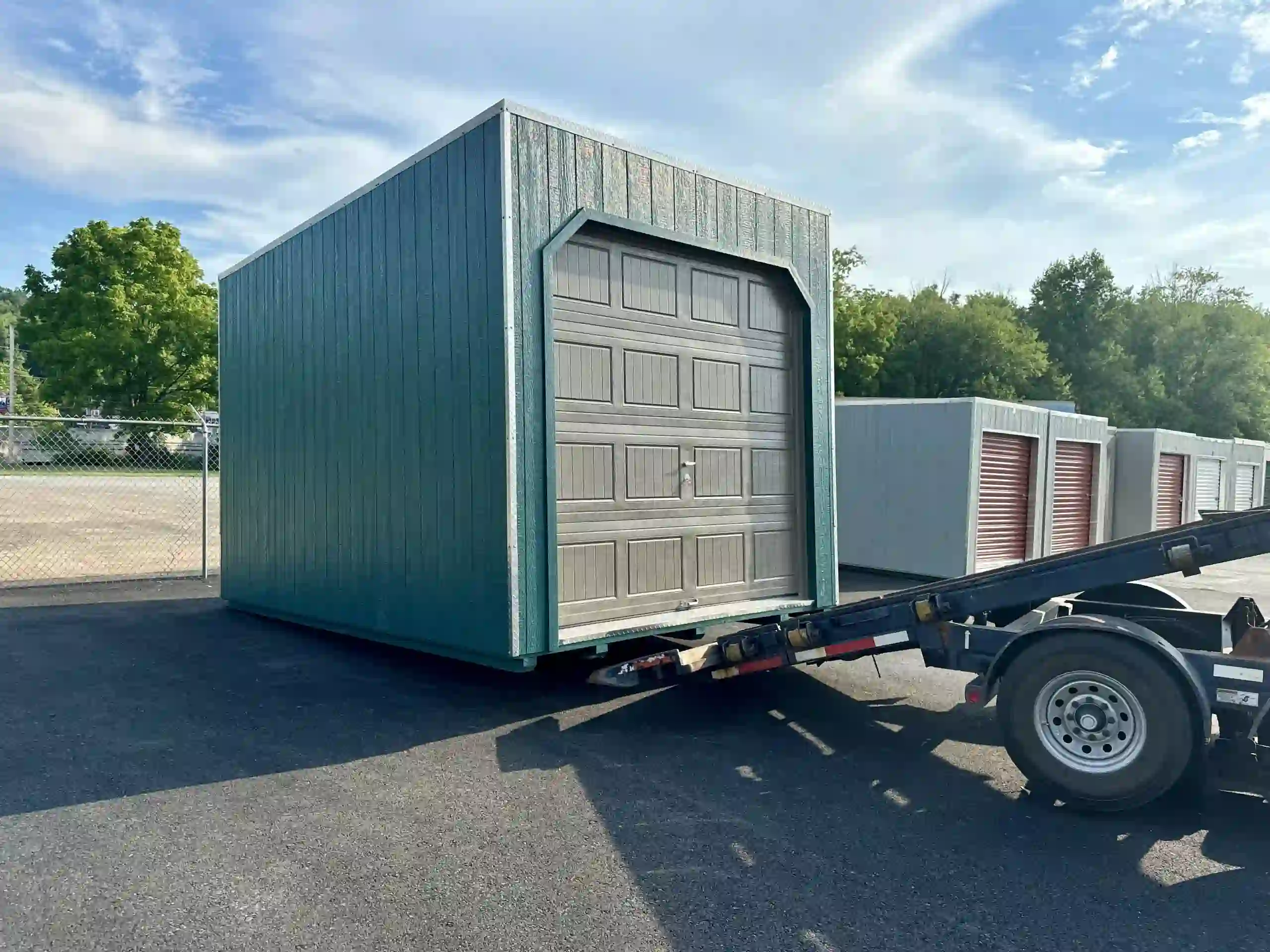 A new green portable garage with a tan overhead door loaded onto a delivery trailer, ready for installation.