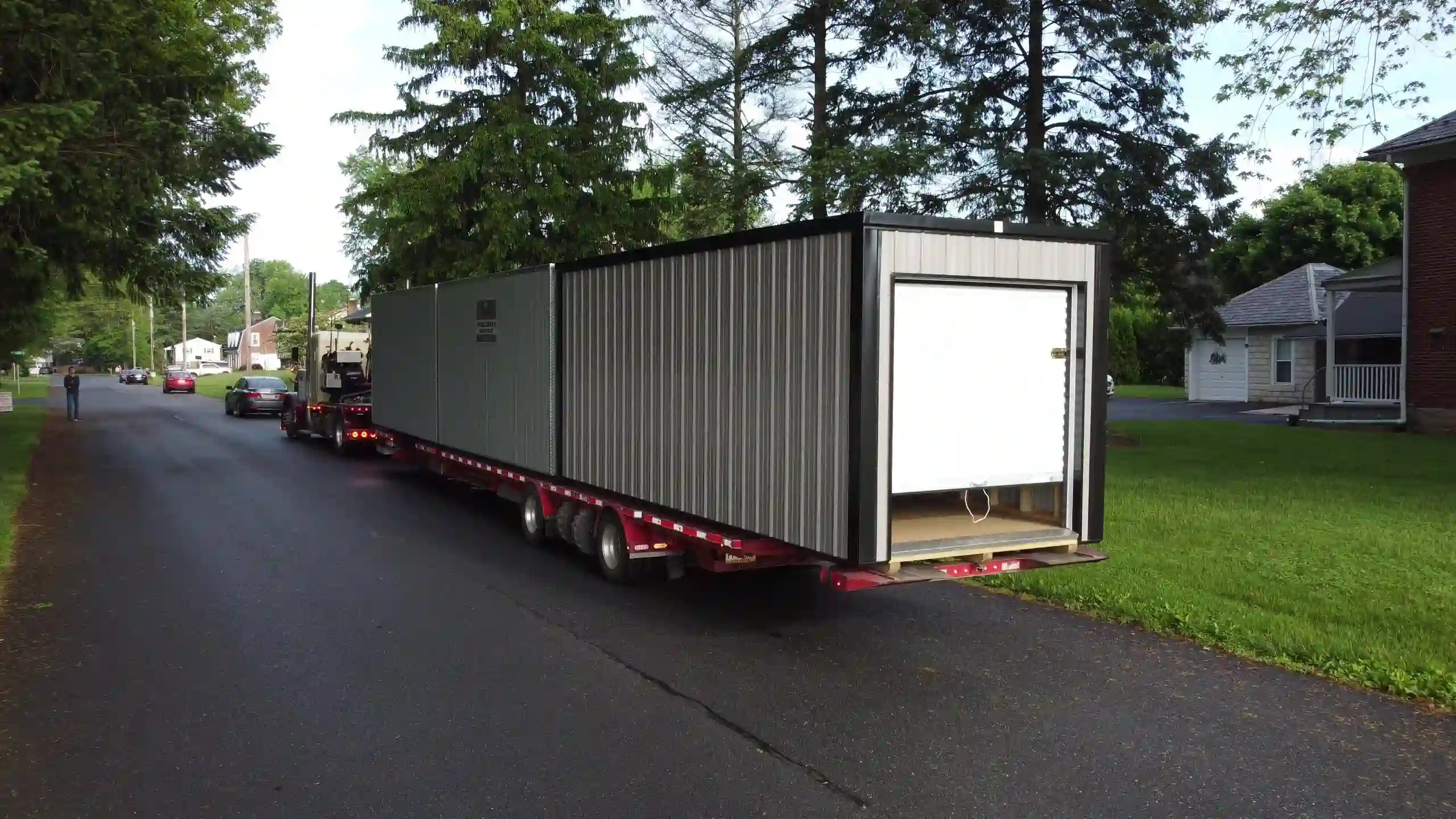 Our long-haul delivery truck carefully navigating a residential street to deliver a large portable storage building to a customer's home.
