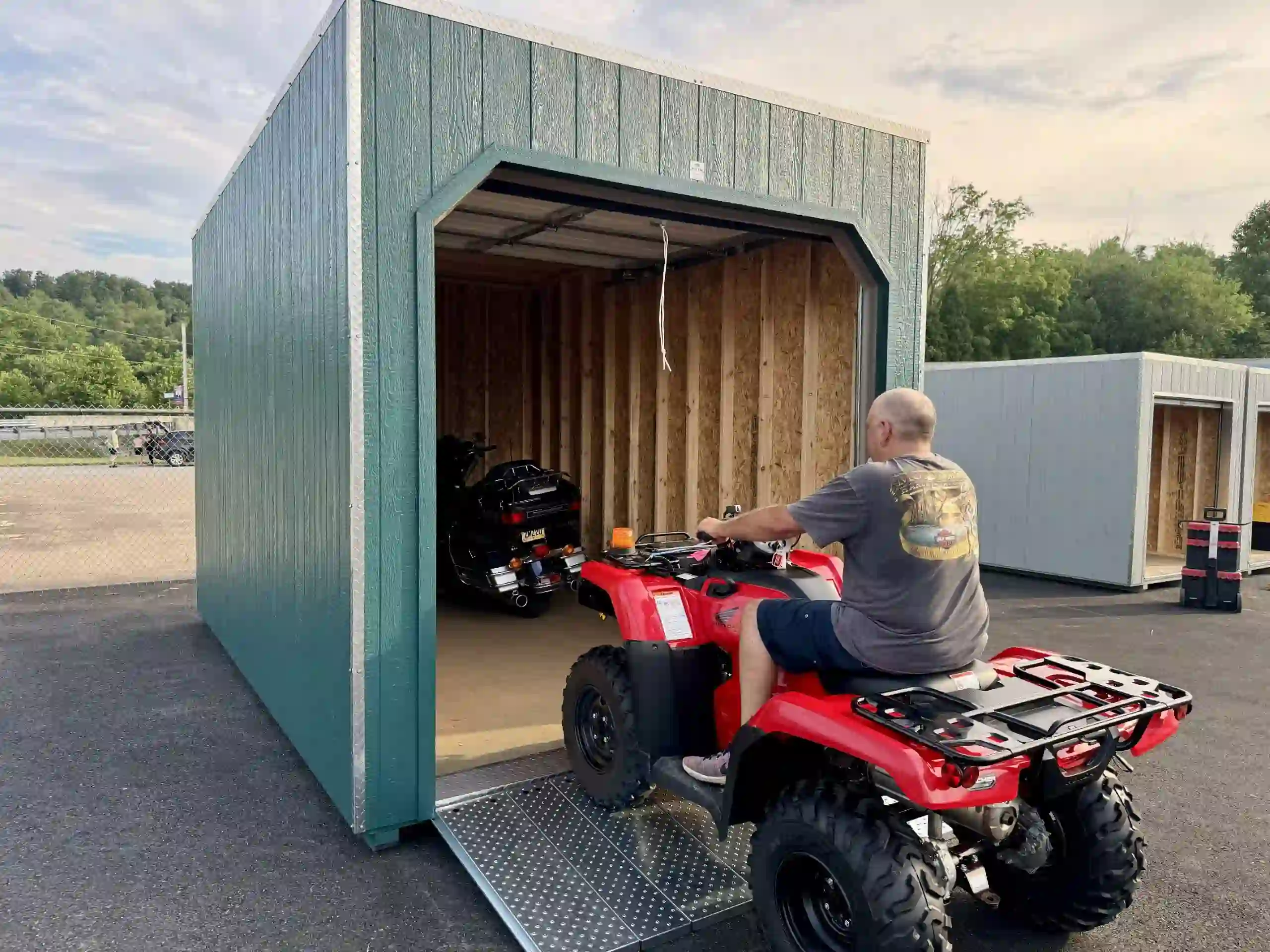 A man driving a red ATV up the ramp into a portable garage, perfect for storing all types of powersports vehicles.