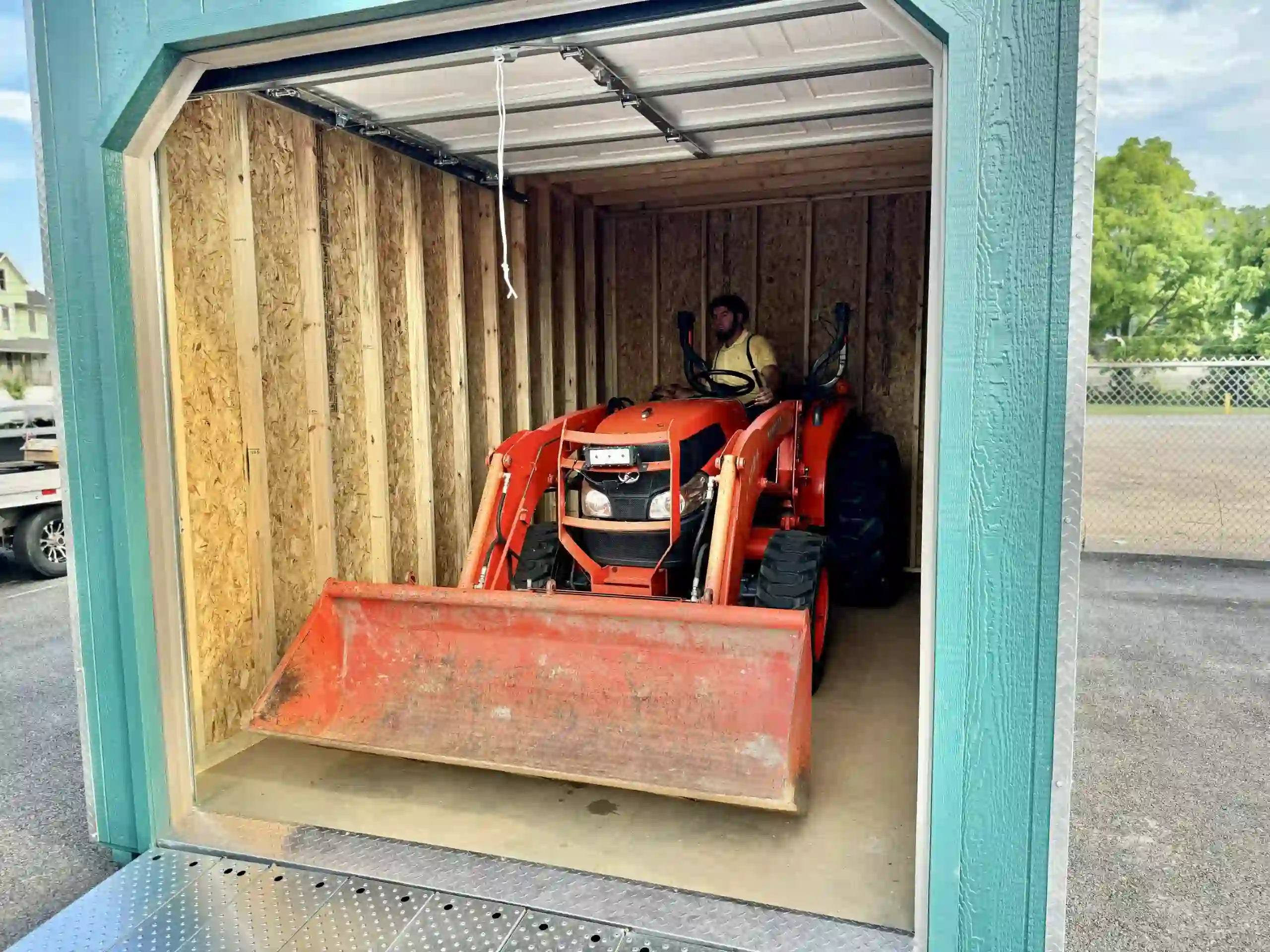 A compact utility tractor with a front-end loader fitting easily inside a heavy-duty portable garage from Mill Run Storage.